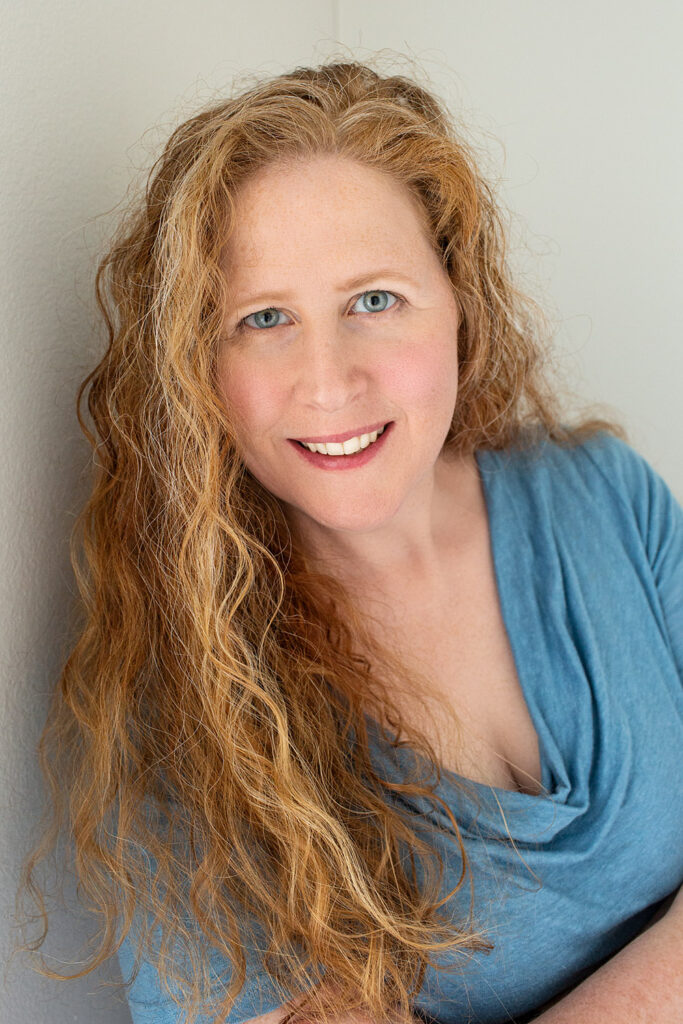 Self-portrait of Jennifer leaning against wall. Long red hair and blue top.