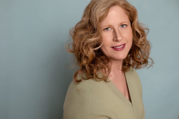 Jennifer smiles warmly at the camera while wearing green top on a green-blue background