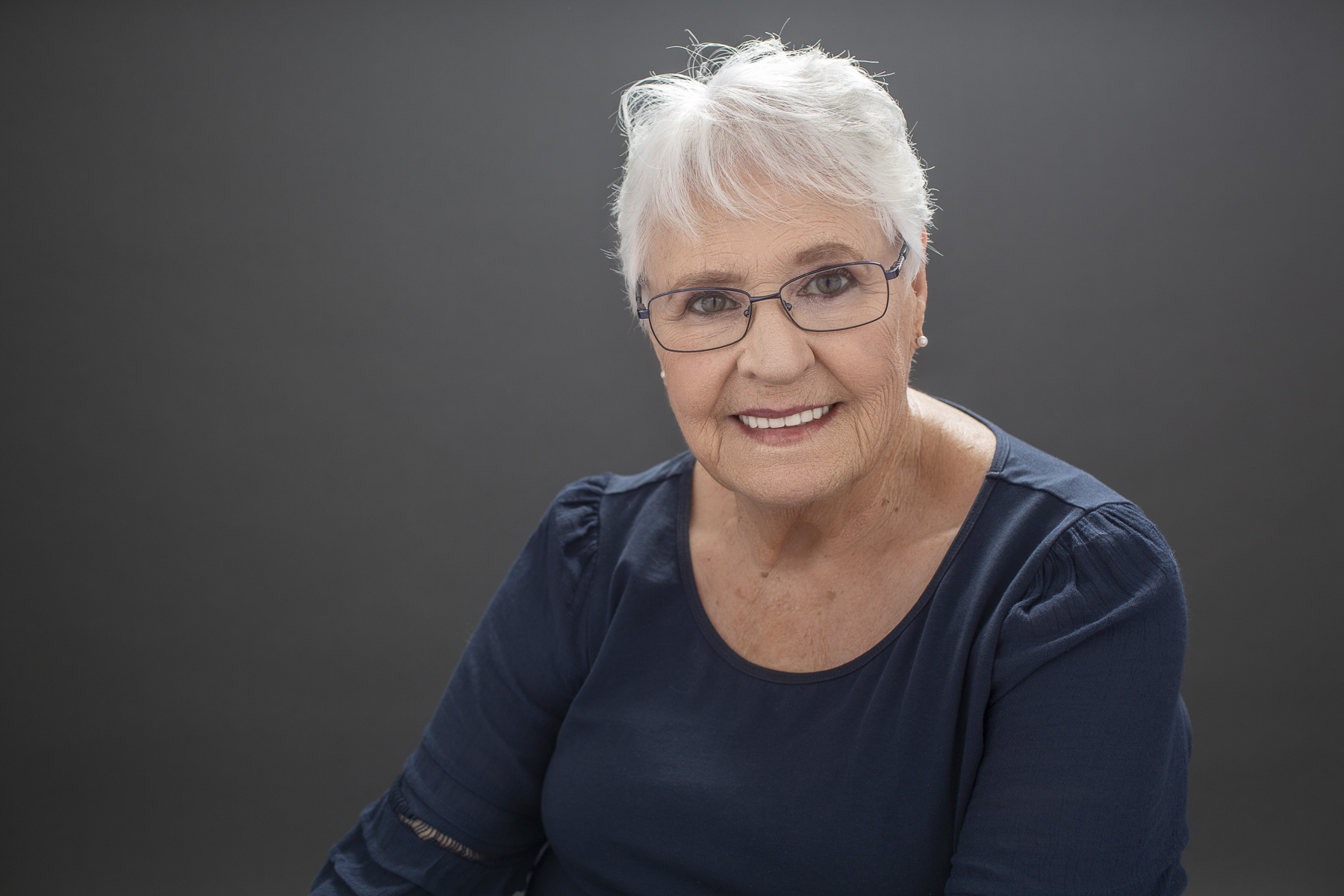 Older woman smiles at camera in backlit portrait created by Redhead Creative Media in Chapel Hill, NC.